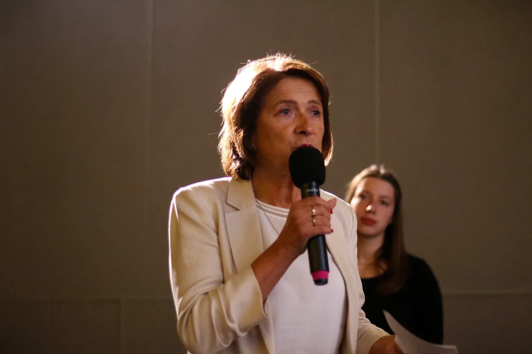 Žena ve světlém saku pokládá kandidátům otázku do mikrofonu
